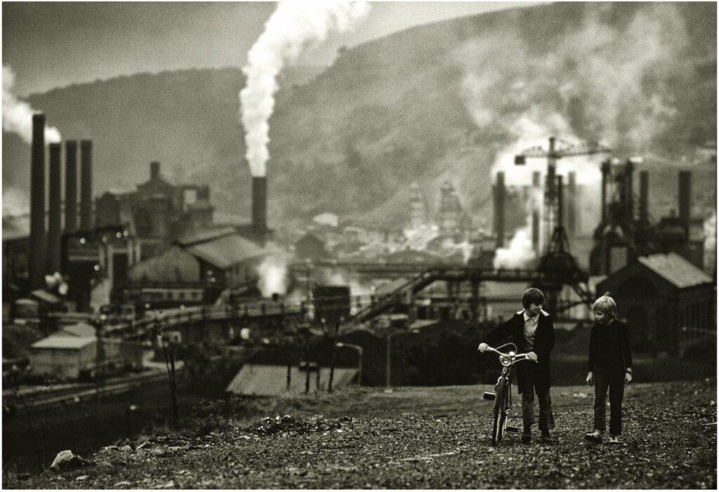 An old photo of two children and there bikes at the top of a hill overlooking a colliery