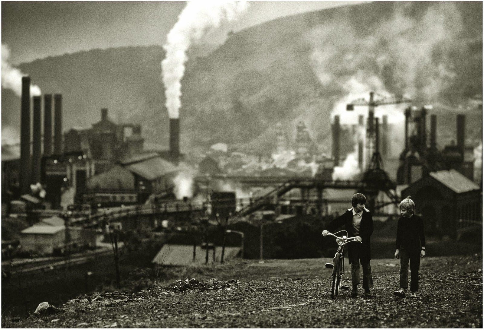 An old photo of two children and there bikes at the top of a hill overlooking a colliery